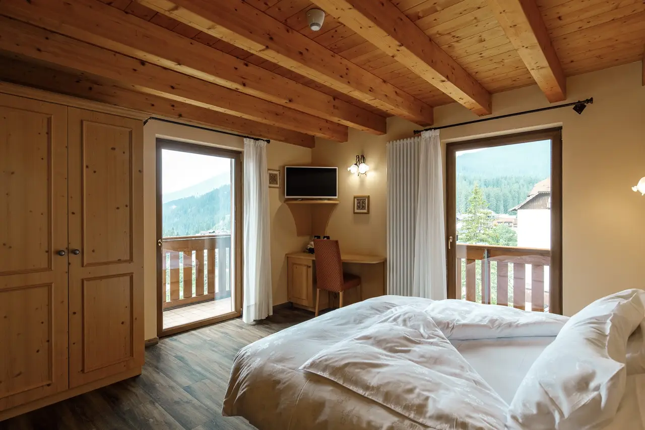 Una camera doppia dell'Hotel Montanara: soffitto con le travi di legno, armadio di legno, due porte finestre aperte sul balcone