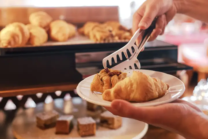 Una mano prende un cornetto con le pinze dal vassoio del buffet