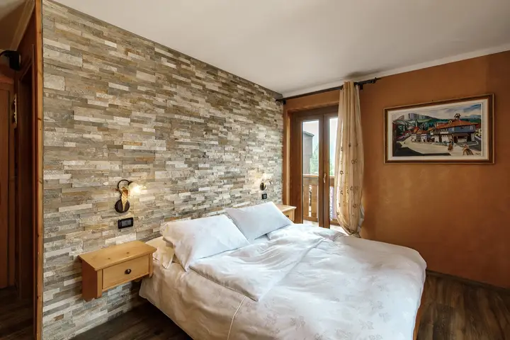 Camera doppia dell'Hotel Montanara: letto matrimoniale davanti alla parete in pietra, porta finestra sul balcone
