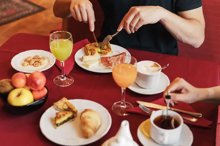 Una colazione al tavolo sulla tovaglia rossa: caffè, succhi, frutta e una fetta di torta