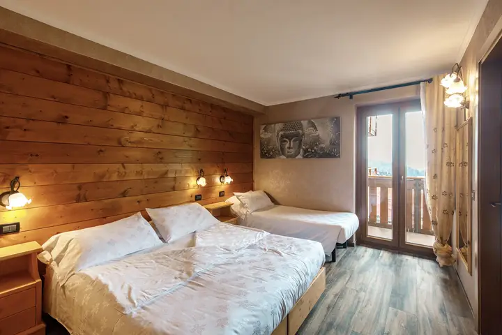 Camera tripla dell'Hotel Montanara: letto matrimoniale e letto singolo, parete di legno, porta finestra sul balcone